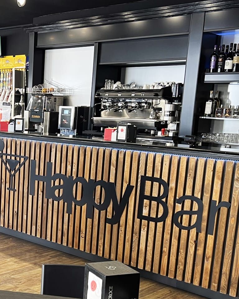 Il bancone dell'Happy Bar con la scritta HappyBar, la macchina espresso e le bottiglie